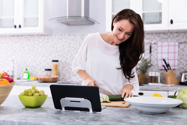 Happy Young Woman Using Digital Tablet While Cooking Food In Kitchen - Foto, Bild
