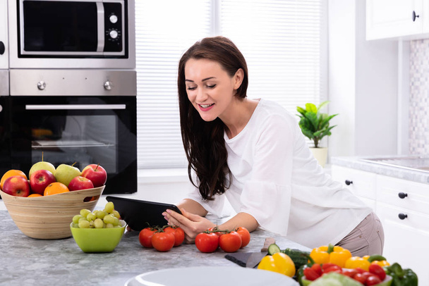 Happy Young Woman Using Digital Tablet Near Fresh Vegetables On Kitchen Counter - Valokuva, kuva