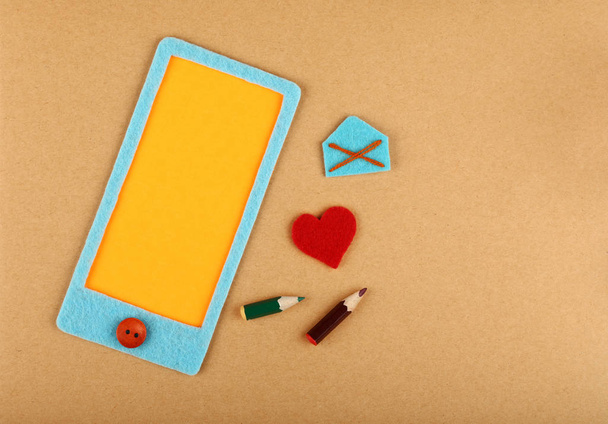 Close up felt craft blue smartphone with yellow blank screen copy space, heart and mail envelope over brown paper background, elevated top view, directly above - Fotoğraf, Görsel