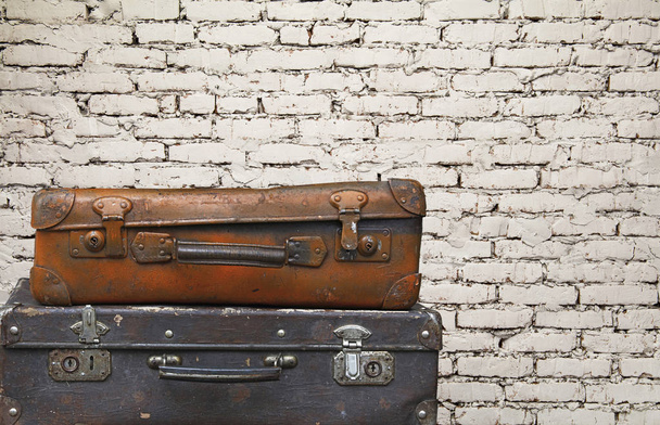 Close up stack of two old vintage antique grunge travel luggage brown leather suitcase trunks isolated over background of white brick wall, low angle side view - Photo, Image
