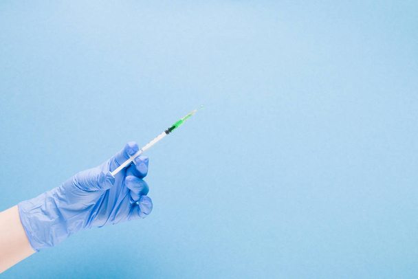 female hand in a blue rubber medical glove holds an insulin syringe with green colored medicine, the vaccine inside on a blue background copy space, treatment and health care concept, diabetes concept - Photo, image
