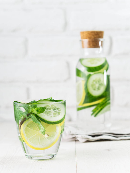 Infused detox water with cucumber, lemon and mint in glass and bottle on white table. Diet, healthy eating, weight loss concept. Copy space - 写真・画像