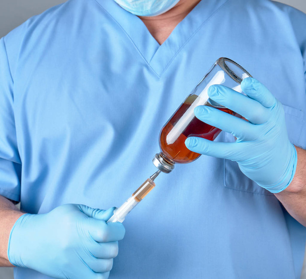 doctor in blue uniform holds a syringe and a glass bottle with injection, close up - Φωτογραφία, εικόνα