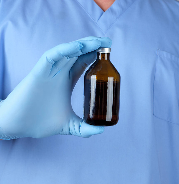 doctor in blue uniform and latex gloves holding a brown glass bottle with medicine for treatment, close up - Foto, Imagem