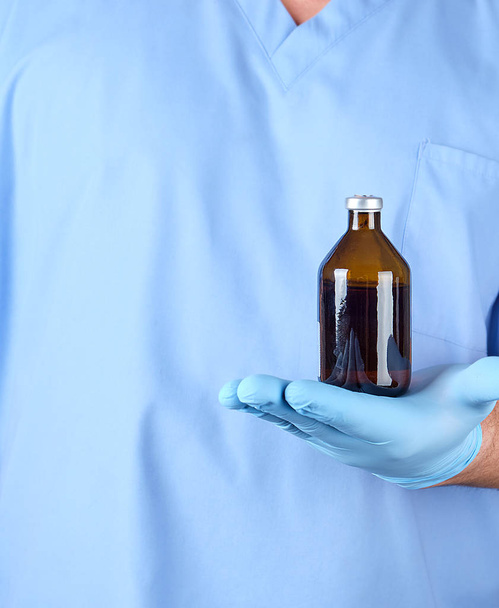 doctor in blue uniform and latex gloves holding a brown glass bottle with medicine for treatment - Φωτογραφία, εικόνα