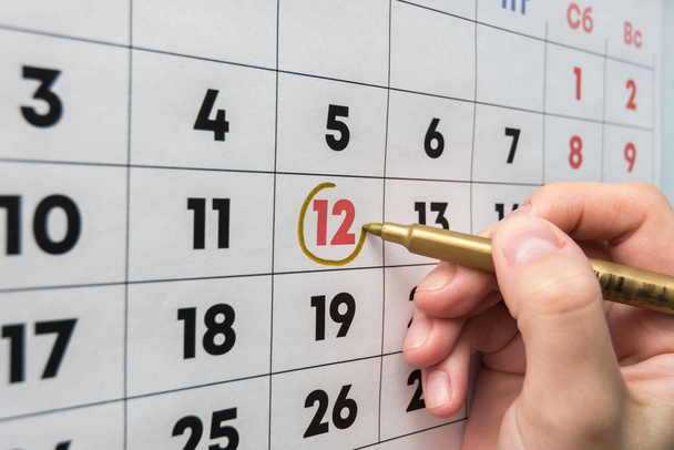 Hand with a marker on the wall calendar leads around a red holiday - Φωτογραφία, εικόνα