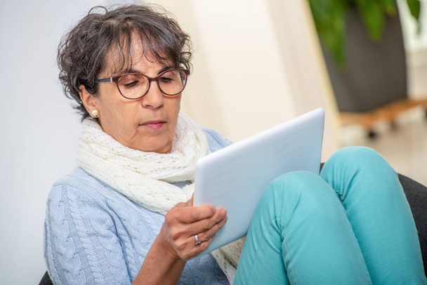 affascinante donna bruna anziana con occhiali utilizzando un tablet digitale a casa
 - Foto, immagini
