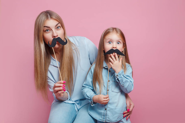 Mother and her daughter girl holding paper mustache on sticks. - Foto, afbeelding