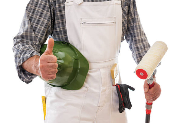 House painter worker in white work overalls with thumb up, holds in his hand the roller to paint. Equipped with protective gloves. Isolated on white background. Construction industry. - Photo, image