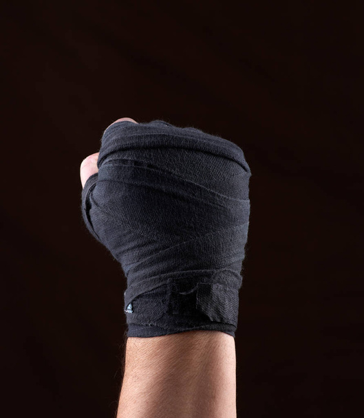 male  hand is wrapped in a black sports textile bandage on a brown  background, copy space - 写真・画像