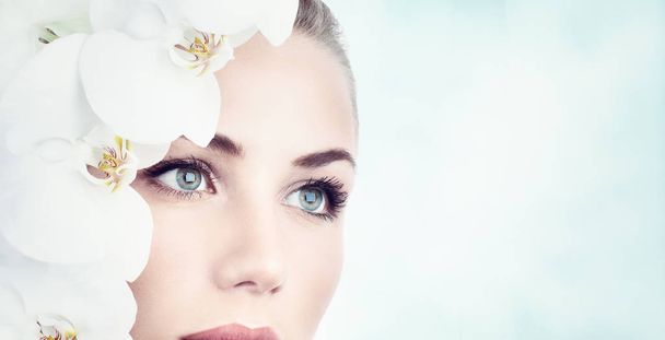 Closeup portrait of a beautiful young woman with white orchids near face over clean background, natural facial cosmetics, day at spa, beauty and health concept. - Foto, Imagem