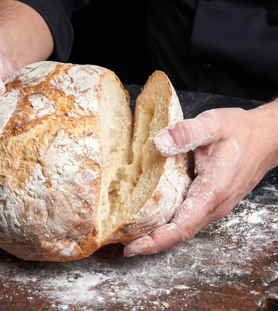 cook in a black tunic holds fresh baked bread, close up - Foto, Bild