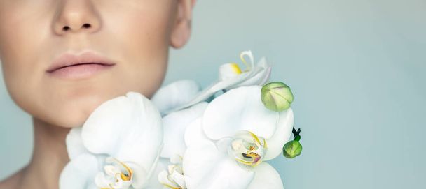 Closeup portrait of a women's face and gentle white orchid flowers isolated on gray blue background, beauty and health treatment, day spa concept - Foto, Imagen