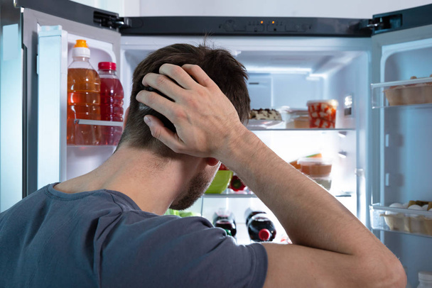 Hämmentynyt mies etsii ruokaa avoimessa jääkaapissa
 - Valokuva, kuva