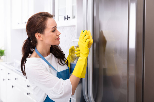 Happy Young Woman Cleaning Refrigerator With Sponge And Bottle Spray - Foto, afbeelding