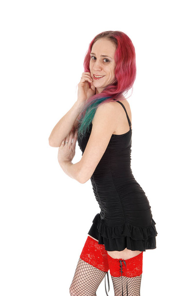 A gorgeous young woman standing in profile in a short black dress and.stockings with her red hair, isolated for white background. - Zdjęcie, obraz