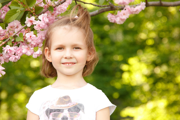 portrait of happy little girl near Japanese cherry tree - Valokuva, kuva
