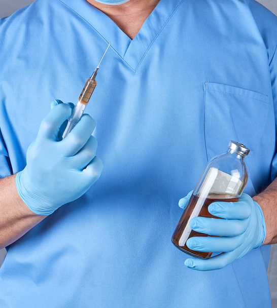 doctor in blue uniform and latex sterile gloves holding a syringe and a glass bottle of vaccine - Φωτογραφία, εικόνα