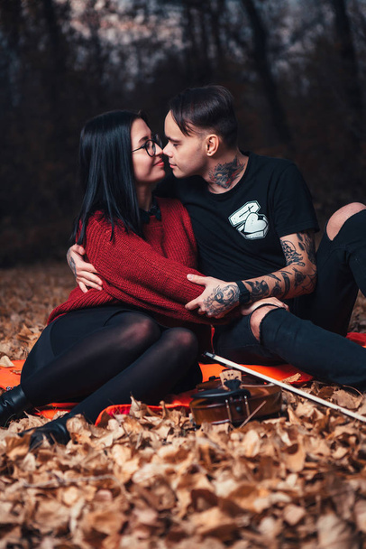 young man and young woman are sitting on a plaid in an autumn forest. - Fotografie, Obrázek
