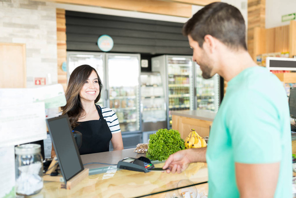 Cajero femenino feliz con el cliente en el mostrador de pago en la tienda de comestibles
 - Foto, Imagen