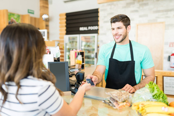 Usmívající se muž pokladní obdrží platbu kreditní kartou v supermarketu - Fotografie, Obrázek