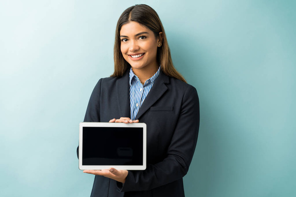 selbstbewusste Geschäftsfrau lächelt, während sie ein digitales Tablet mit leerem Bildschirm vor blauem Hintergrund hält - Foto, Bild