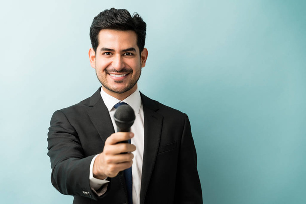 glücklich gut aussehender männlicher Profi im Anzug gibt Mikrofon im Stehen im Studio - Foto, Bild