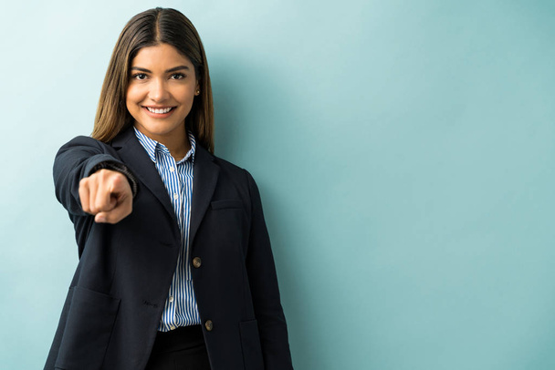 Confident gorgeous young businesswoman pointing finger while standing against blue background - Foto, afbeelding