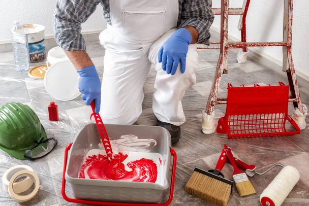 Caucasian house painter worker in white work overalls, mixes the paint in the container. Construction industry. - 写真・画像
