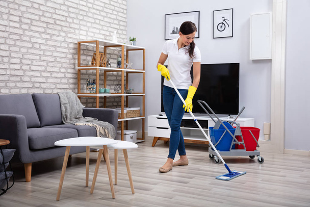 Hausmeisterin putzt Fußboden mit Wischmopp im Wohnzimmer - Foto, Bild