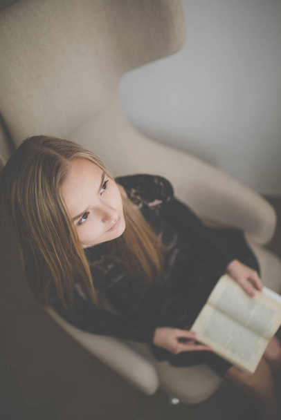 Cute young woman reading a book in a designer chair - color toned image, shallow DOF - Foto, Imagen