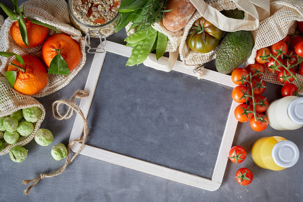 Fresh organic groceries packed in eco-friendly reusable fabric bags. Recipe or menu layout concept with white frame on grey background, viewed from above - Φωτογραφία, εικόνα