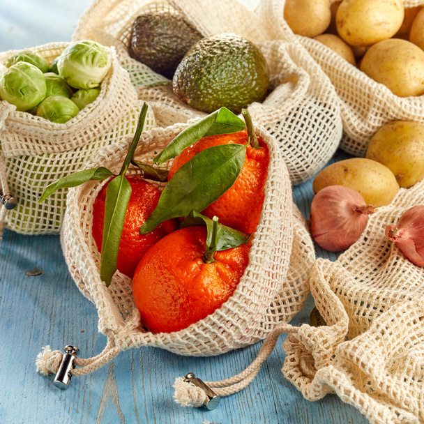 Verse groenten en fruit uit de lokale markt verpakt in milieuvriendelijke herbruikbare netzakken, van dichtbij bekeken op houten ondergrond - Foto, afbeelding
