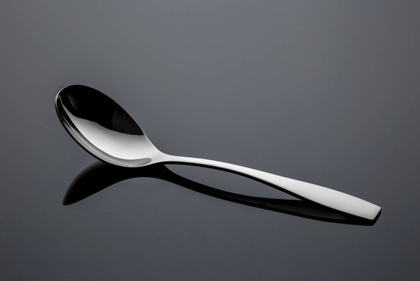 Stainless steel metal spoon on a reflective surface - Fotoğraf, Görsel