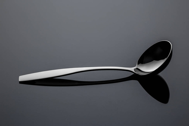 Stainless steel metal spoon on a reflective surface - Valokuva, kuva
