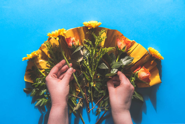 Woman's hands picking flowers from an unwrapped bouquet of flowers, tabletop view with a blue background - Foto, immagini