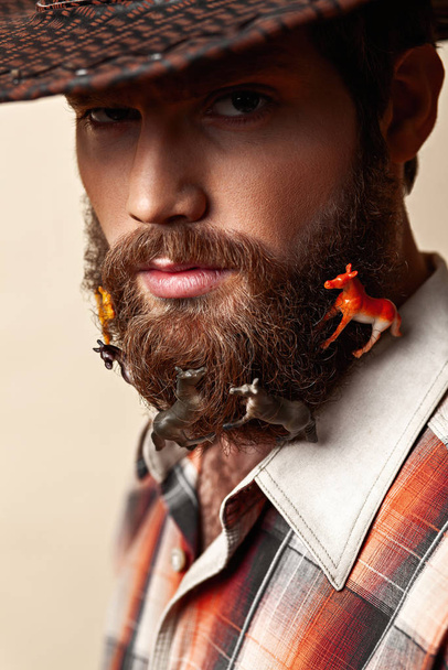 Young man in a cowboy hat and toy horses in a beard - Photo, image