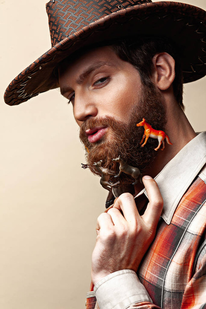 Young man in a cowboy hat and toy horses in a beard - Foto, Bild