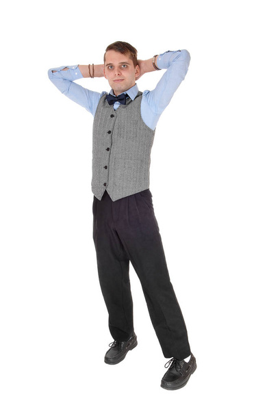 A young tall businessman standing in a gray vest and bow tie with his.hands behind his head, isolated for white background. - Fotografie, Obrázek