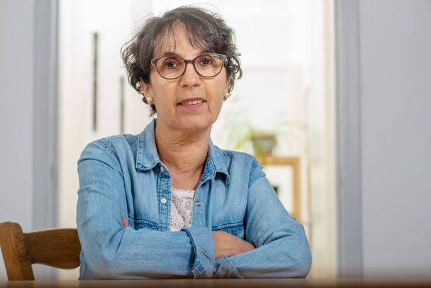portrait of senior brunette with a blue jeans jacket and glasses at home - Foto, Imagem