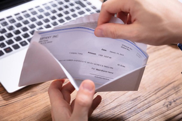 Elevated View Of Person's Hand Removing Paycheck From The Envelope Over Wooden Desk - Foto, Imagem
