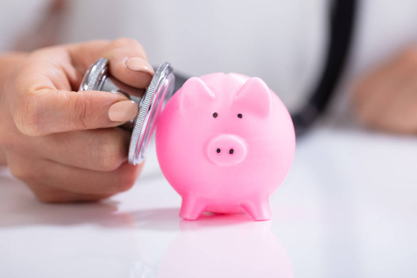 Close-up Of Doctor's Hand Examining Pink Piggybank With Stethoscope - Foto, imagen