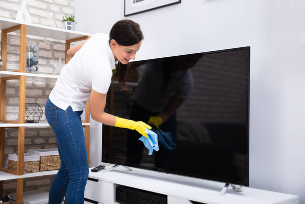 Zbliżenie: kobieta za pomocą ściereczki do czyszczenia telewizora w domu - Zdjęcie, obraz