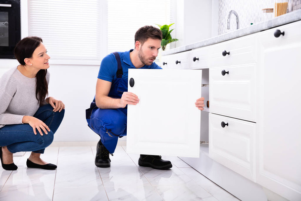 Woman Looking At Male Handyman Installing Cabinet Door In The Kitchen - 写真・画像
