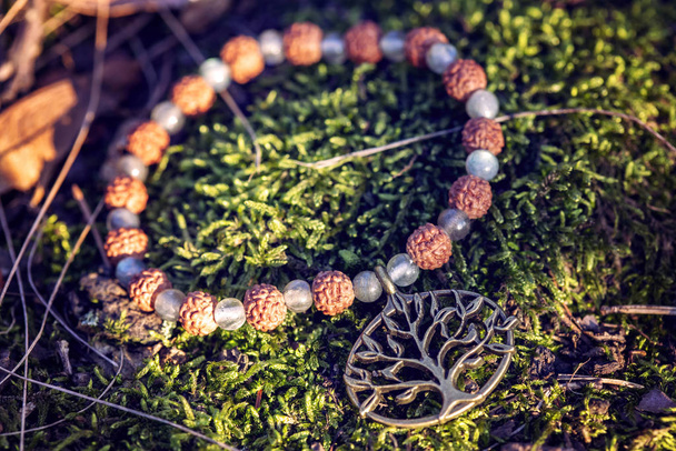 Ciondolo in metallo albero con semi naturali e labradorite perline di pietra minerale sul braccialetto di yoga sullo sfondo della foresta
 - Foto, immagini
