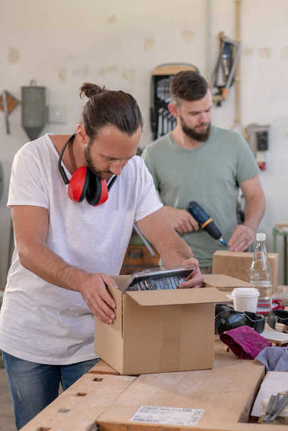 two men in workwear in a carpenter's workshop with parcel - Foto, Imagen