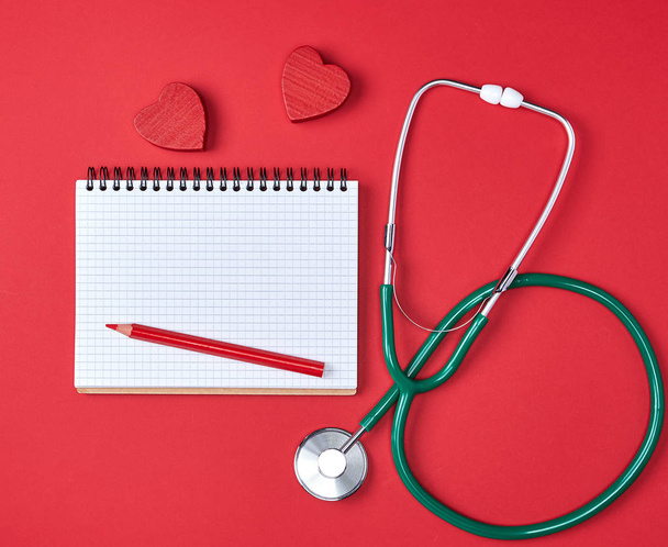 open blank notepad and green medical stethoscope on red background, health care concept - Фото, изображение