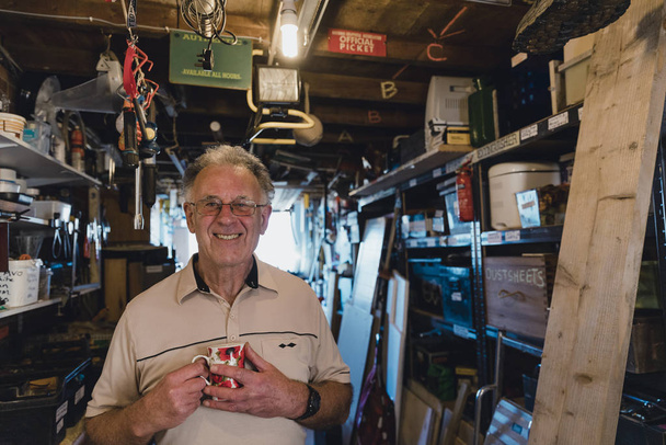 Portrait of a cheerful senior man in his workshop shed with a cup of tea. - Foto, imagen