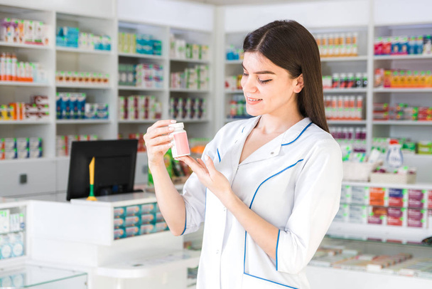 atrakcyjna kobieta farmaceuta z delikatnymi dłońmi trzymając mały słoik z lekiem lub witaminami w aptece - Zdjęcie, obraz