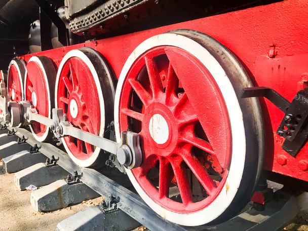 Grandes ruedas de hierro de un tren rojo y negro de pie sobre raíles y elementos de suspensión con muelles de una antigua locomotora de vapor industrial
 - Foto, imagen